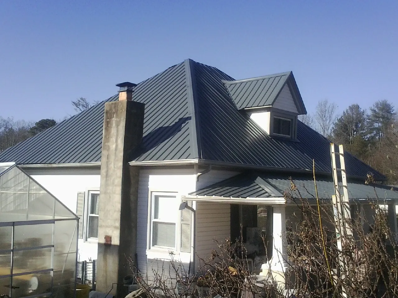 Dark blue standing seam metal roof on a white farmhouse with dormer — Slate & Tile Roof Repair by Roofing Brothers in Taloga