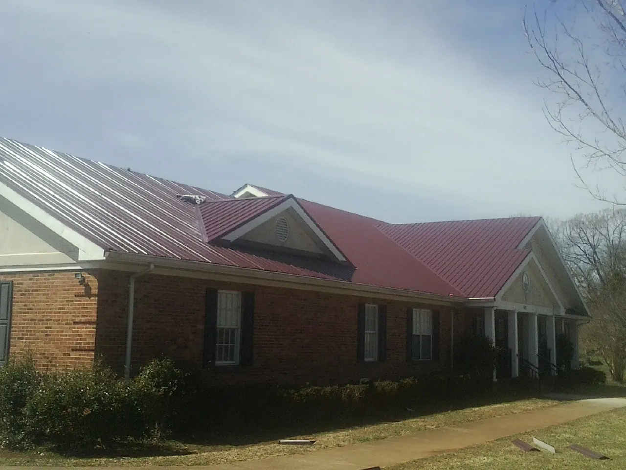 Red metal roof with gabled entries on a long brick building, from a Hail Damage Roof Repair job in Taloga