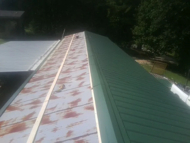 Old rusted panels beside newly installed green metal roofing — Wind Damage Roof Repair by Roofing Brothers in Taloga