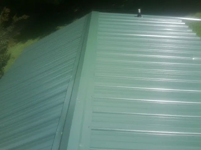New green metal panels meeting at the ridge of a roof — Flat Roof Repair work by our crew in Taloga