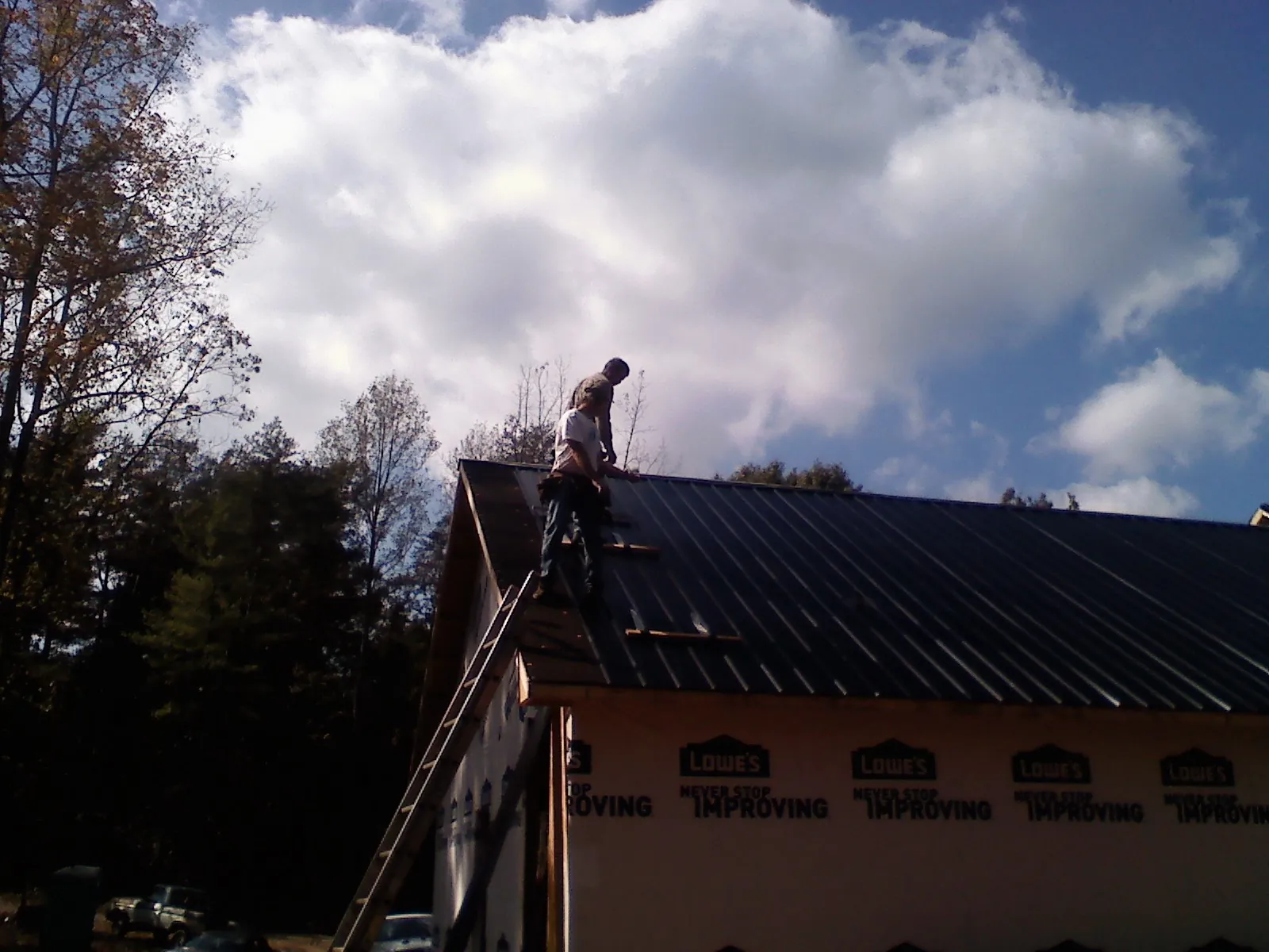 Roofer fastening dark metal panels high against a cloudy sky, from a Roof Inspection job in Taloga