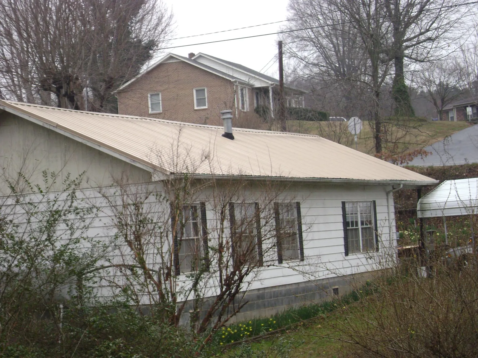 Tan metal roof on a white sided house set into a hillside — Commercial Roofing by Roofing Brothers in Taloga