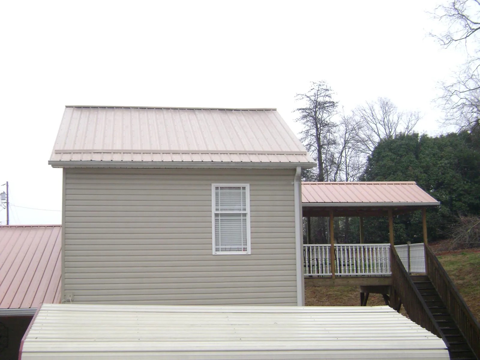 Tan metal roofs on a two story addition and attached porch, from a Roof Replacement job in Taloga